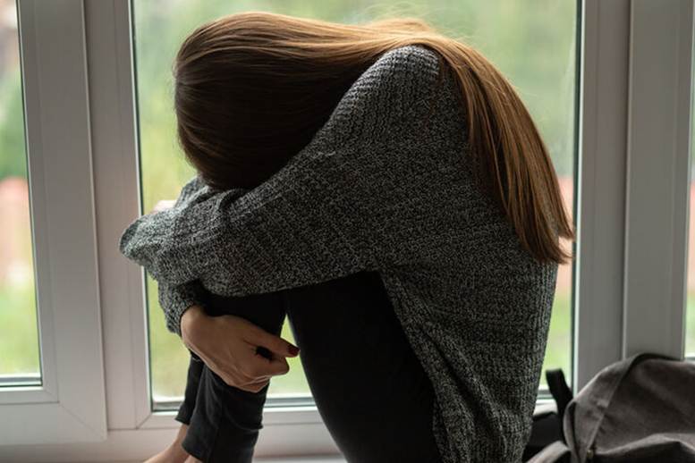 Woman huddled up by window - Sexual Harassement